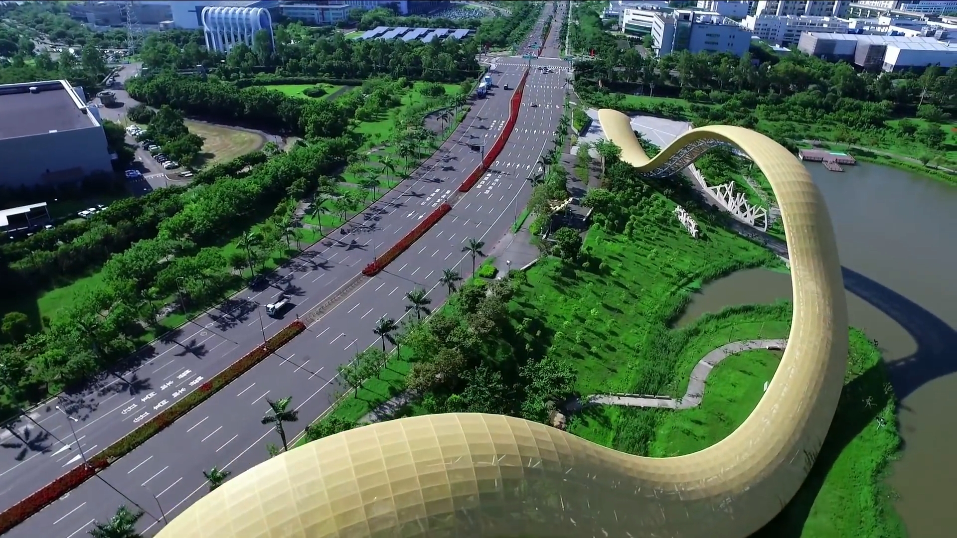南部科學園區空拍景觀：園區主要道路車流穿越兩側綠帶，右側為湖畔金色波浪造型景觀建築